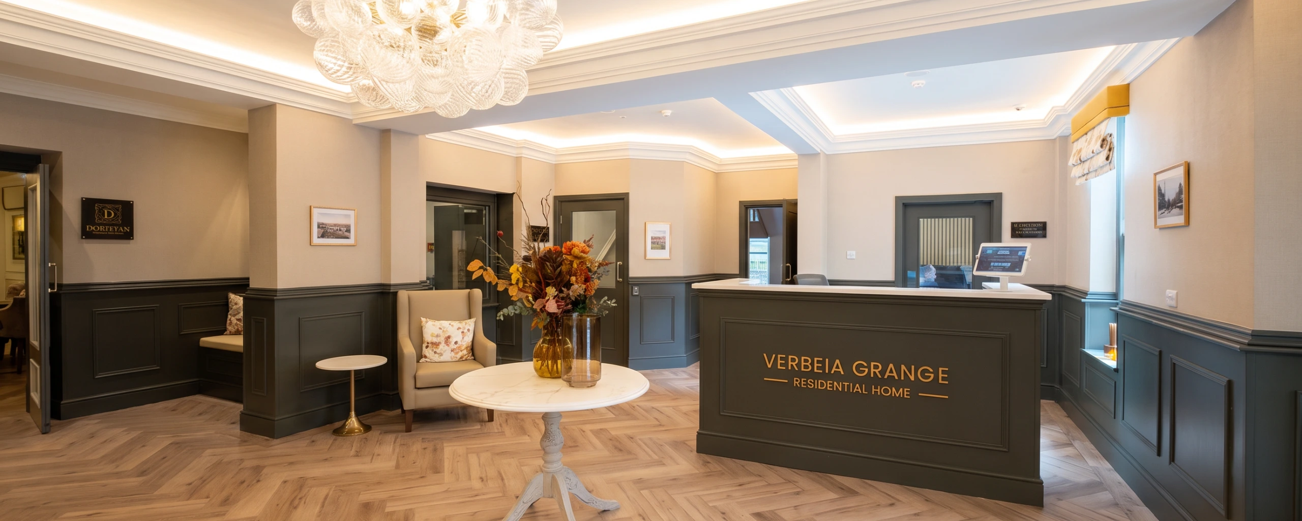 Reception area at Verbeia Grange Residential Home, Ilkley, with a panelled front desk, a chandelier and a herringbone timber floor